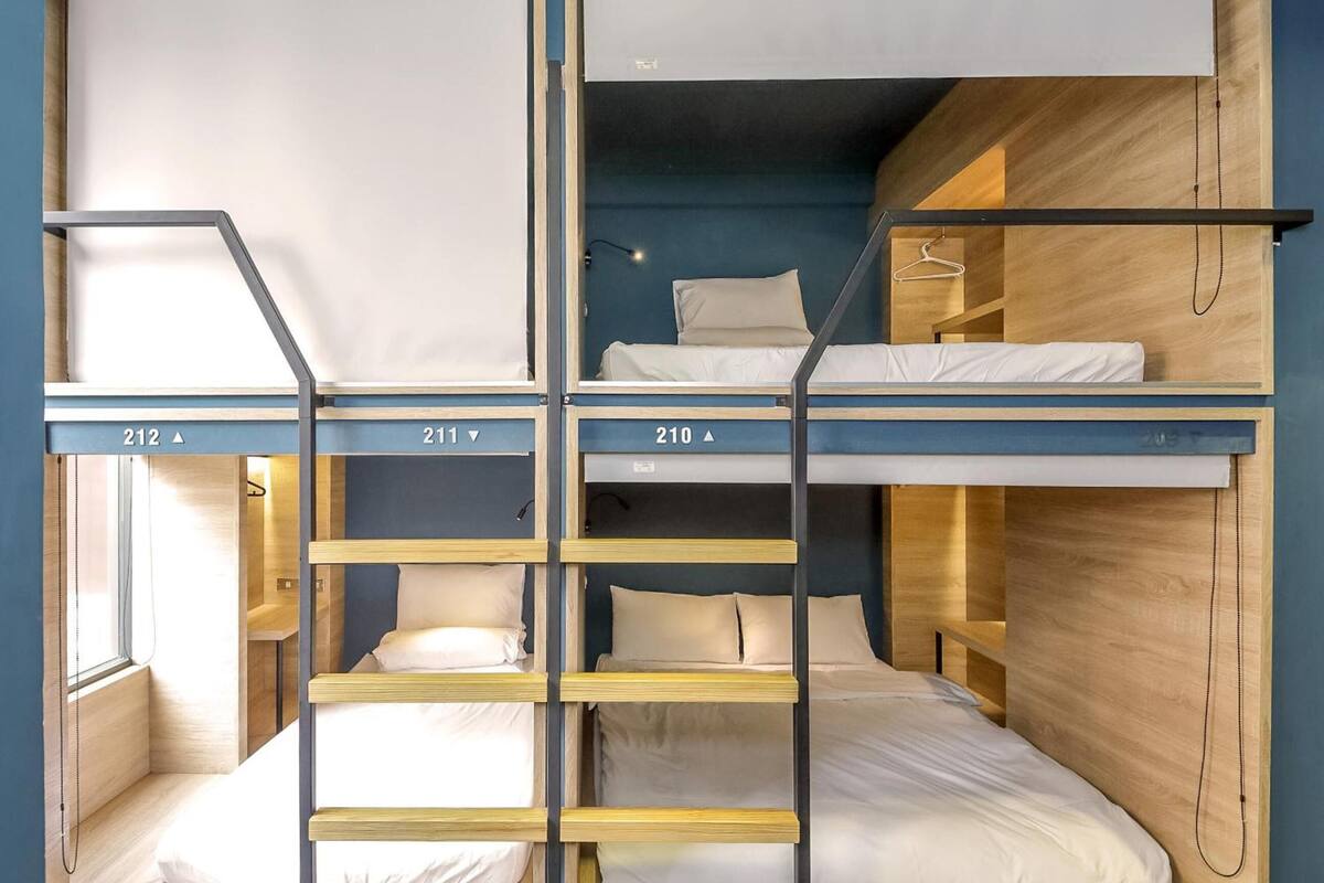 A dormitory-style room with bunk beds, numbered beds, and a window providing natural light.