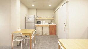 A compact kitchen with a refrigerator, microwave, and sink. There is a wooden table with chairs and a small cabinet with a microwave above it. - DONGMEN 3 Capsule Inn - Hostel (Taipei)