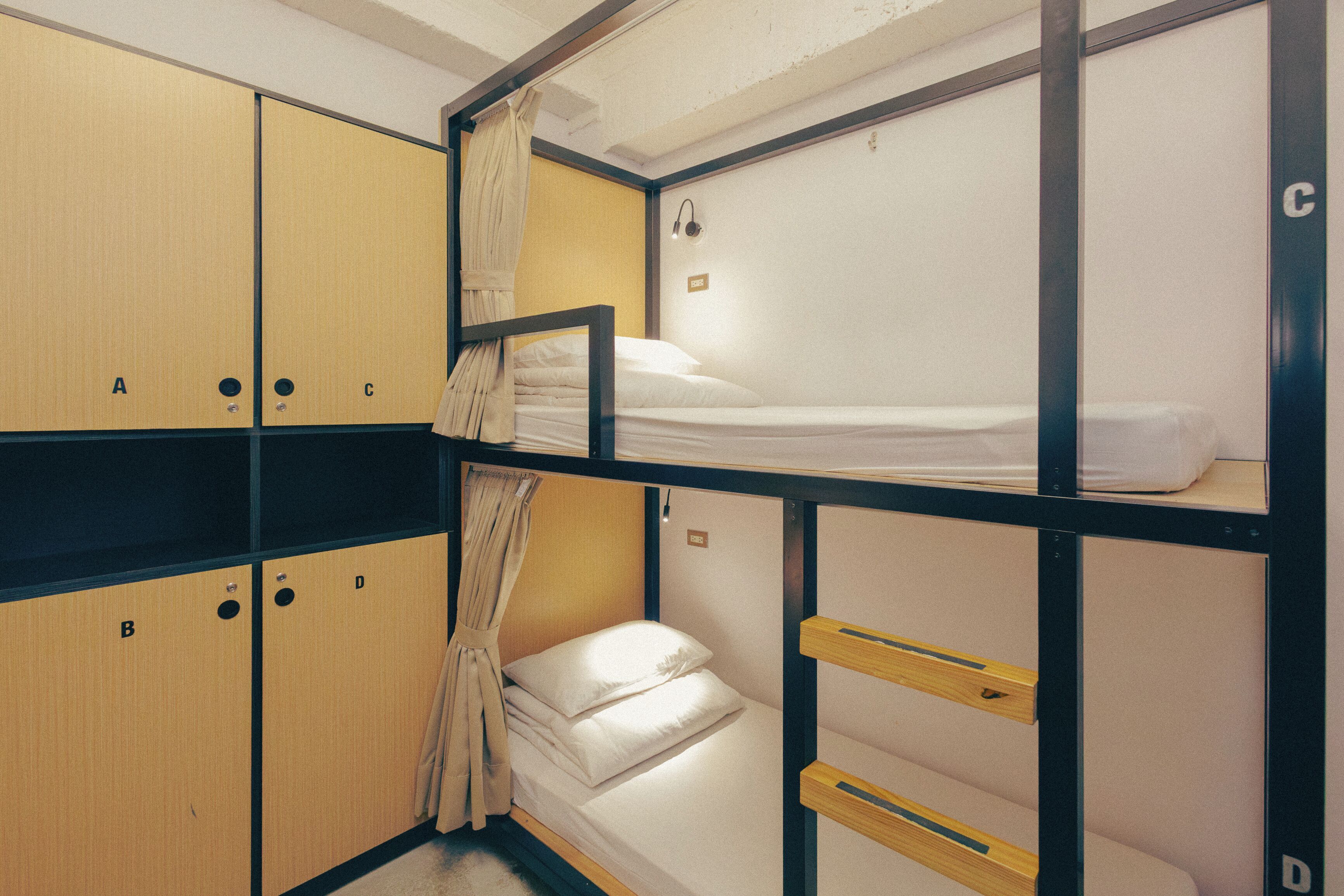 Dormitorio con literas y taquillas de madera identificadas con las letras A, B, C y D, además de una pequeña mesita de noche.