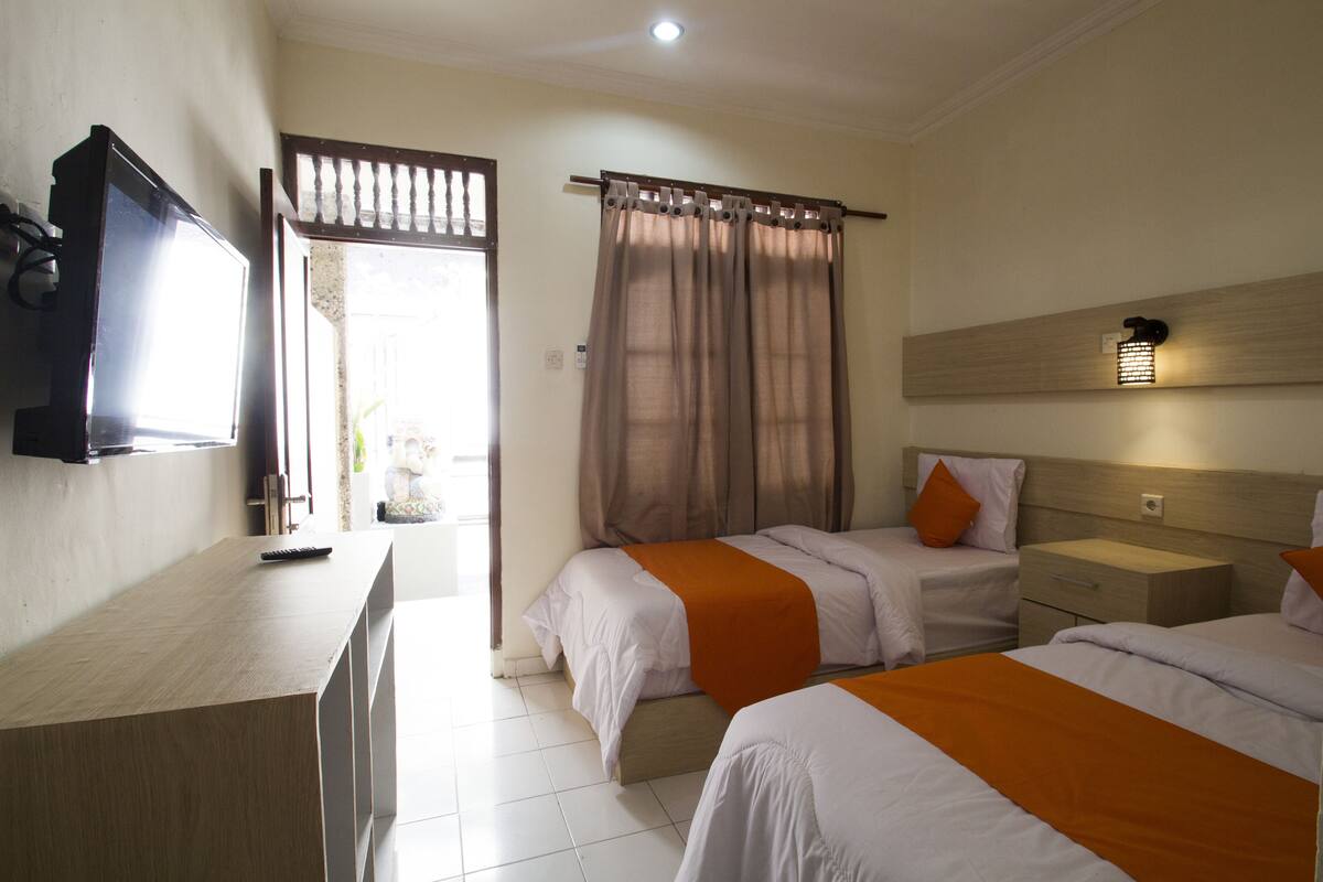 A hotel room with two beds, a TV, a desk, and a window with curtains.