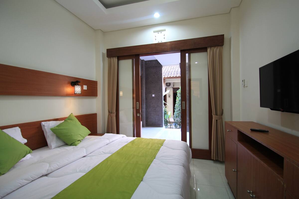 A hotel room with a bed, a TV, a wooden cabinet, and a sliding glass door leading to an outdoor area.