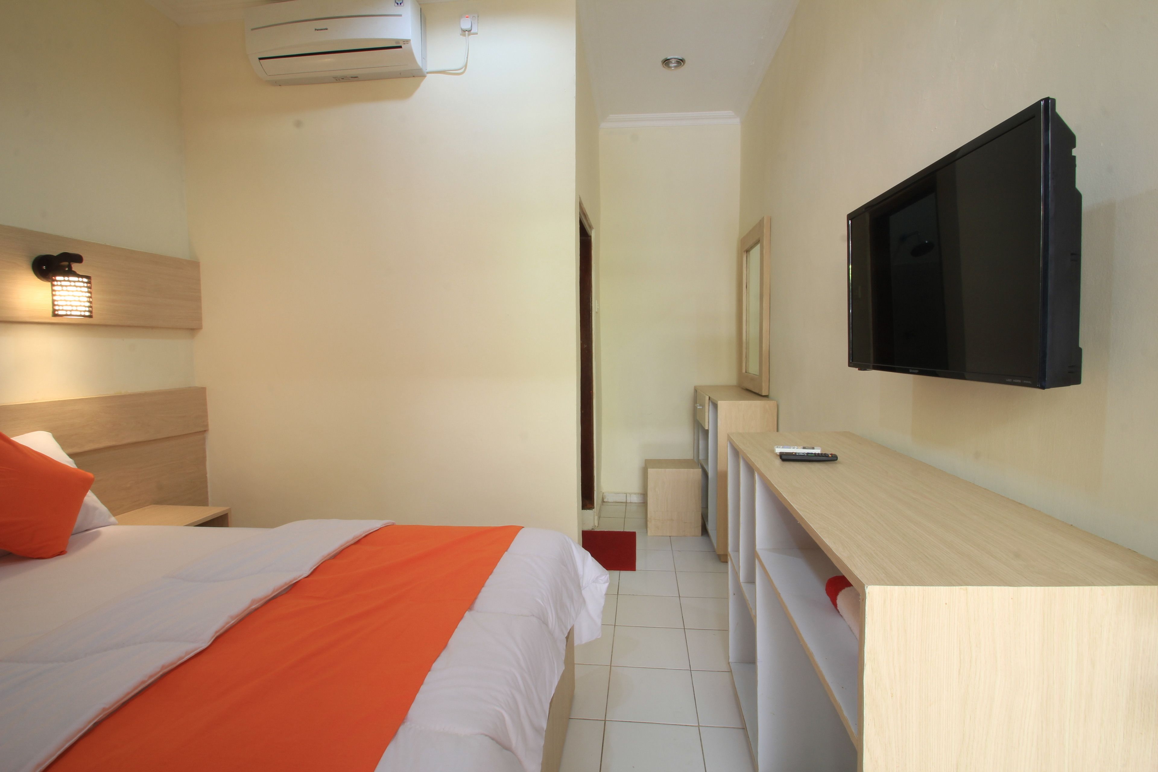 Habitación de hotel con cama, televisión montada en la pared, escritorio y un mueble pequeño.