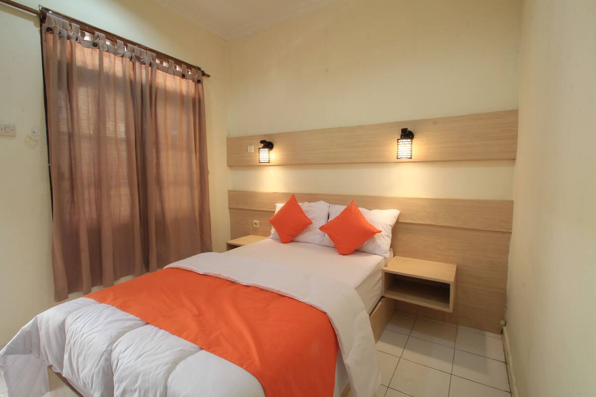 A hotel room with a bed, two nightstands, a wooden headboard, and a window with curtains.