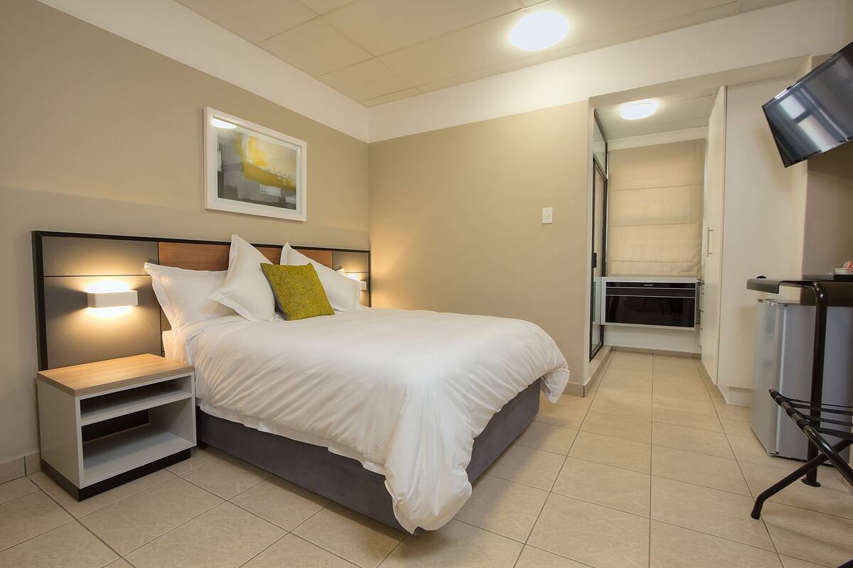 A modern bedroom with a bed, bedside tables, a flat-screen TV, and a walk-in closet.