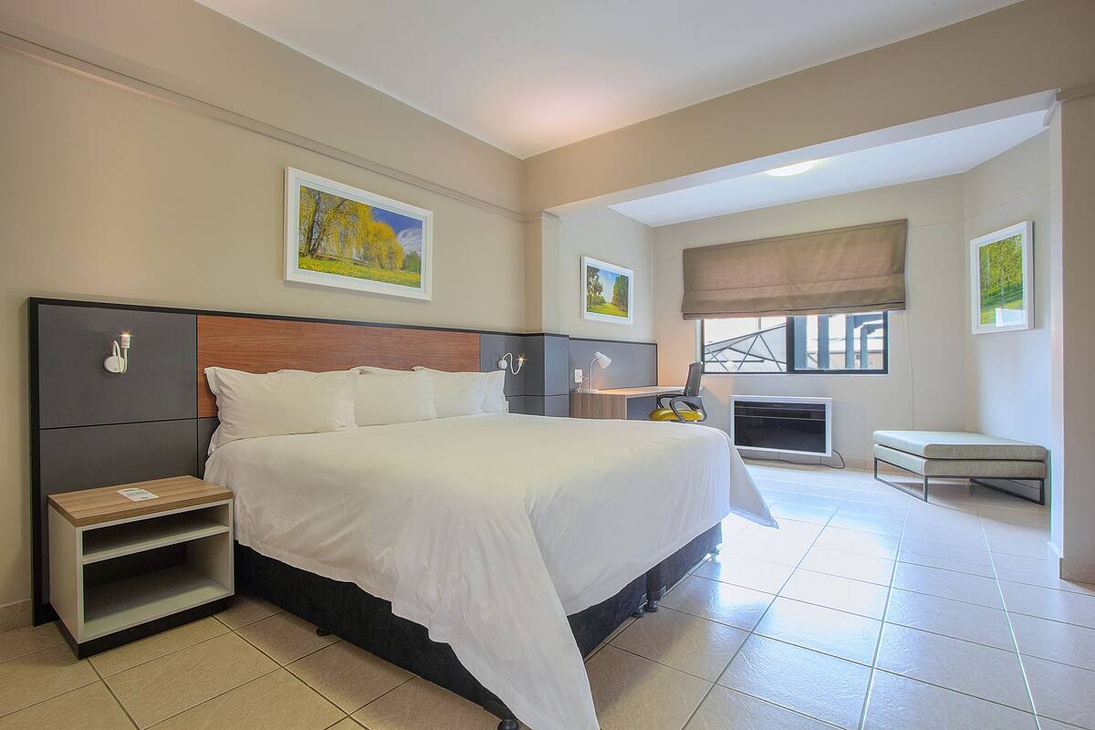 A hotel room with a large bed, a bedside table, a chair, and a window with a view.