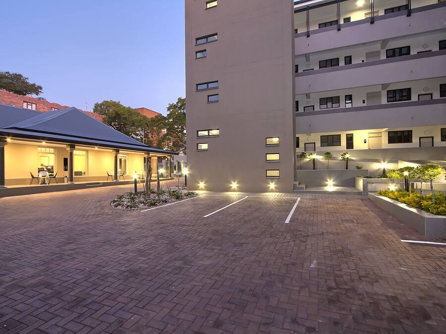 A well-lit courtyard with a modern building, paved walkways, and outdoor seating areas.