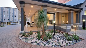A covered outdoor area with a seating arrangement, a central plant, and a modern building in the background. - The Park Lodge Hotel (Pretoria)
