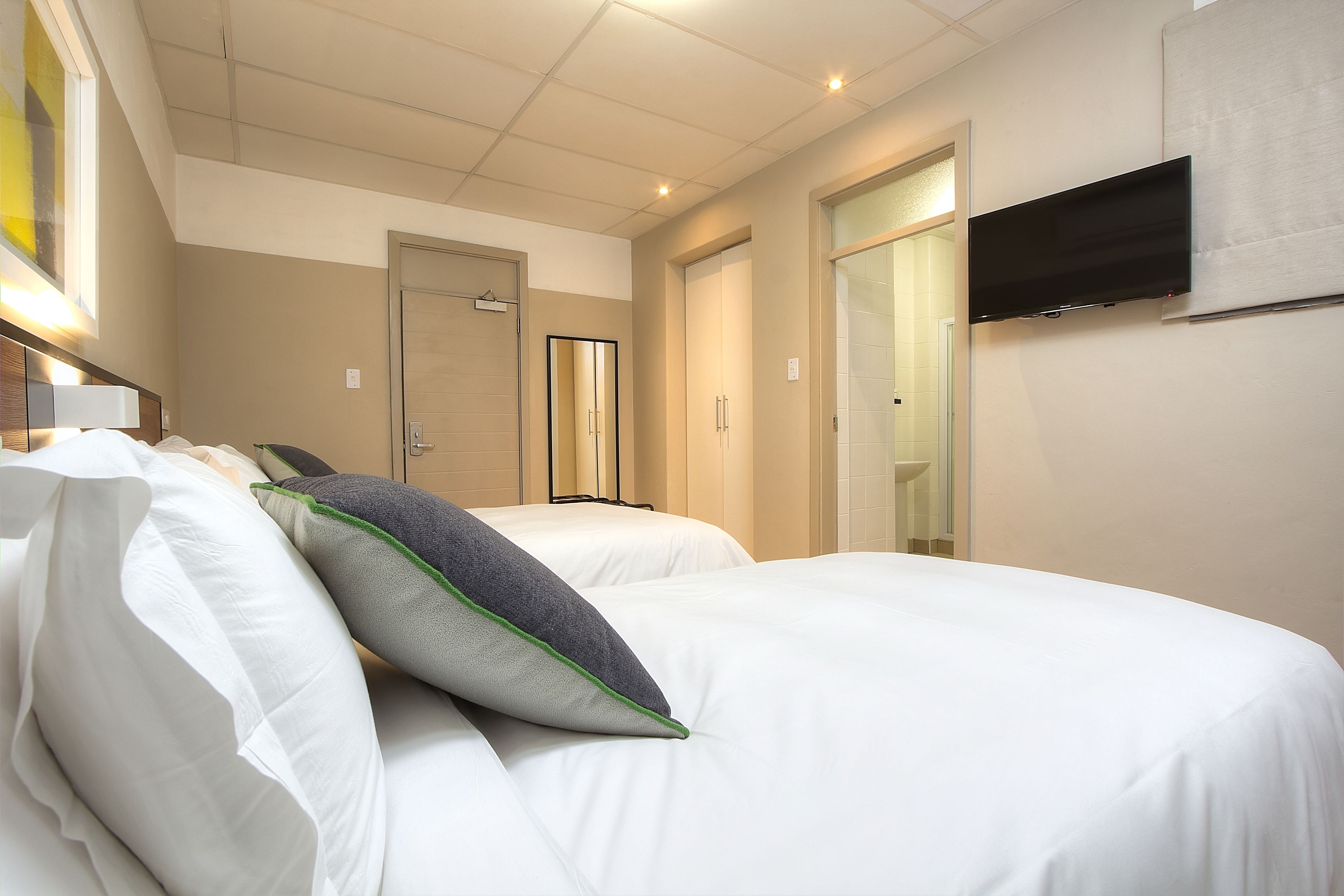 A hotel room with two beds, a flat-screen TV mounted on the wall, and a mirror above the beds.