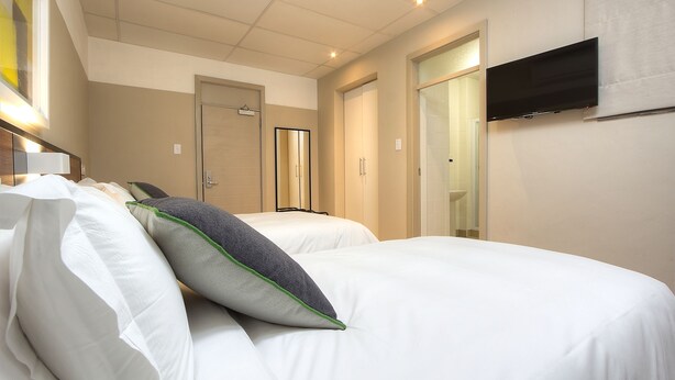 A hotel room with two beds, a flat-screen TV mounted on the wall, and a mirror above the beds. - The Park Lodge Hotel (Pretoria)