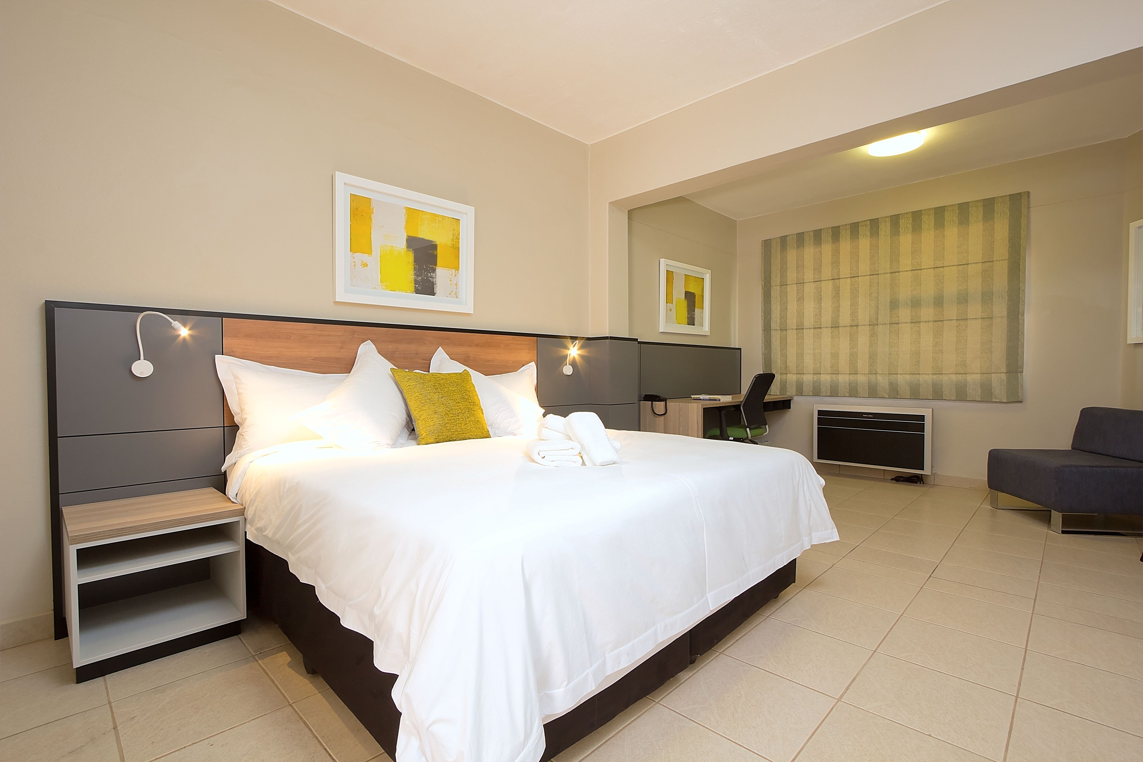 A hotel room with a large bed, a bedside table, a chair, a desk, and a large window.
