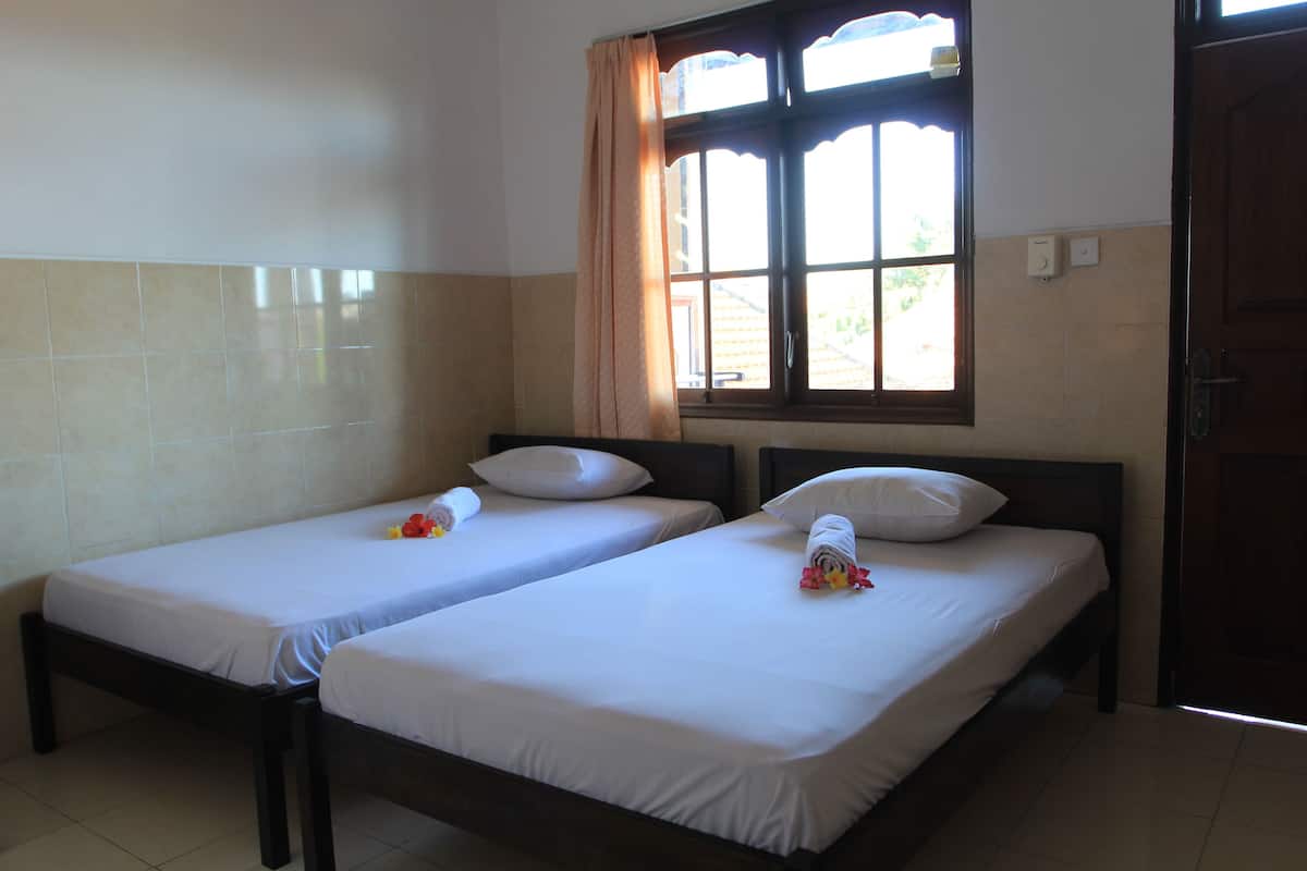 Two single beds with white linens, a window with curtains, and a door.