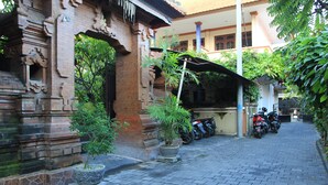 A paved courtyard with a brick building, potted plants, and parked motorcycles. - Losmen Cempaka 3 (Kuta)