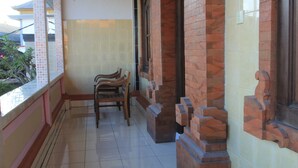 A balcony with tiled flooring, wooden benches, and a brick wall with decorative elements. - Losmen Cempaka 3 (Kuta)