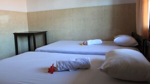 Two single beds with white linens, a small table, and a wall with beige tiles. - Losmen Cempaka 3 (Kuta)