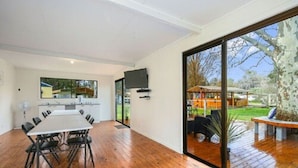 A modern kitchen with a large dining table and chairs, a built-in oven, and a TV mounted on the wall. - Yea Riverside Caravan Park (Yea)