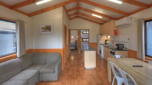 A compact RV interior with a sofa, kitchenette, and a small dining area. - Yea Riverside Caravan Park (Yea)