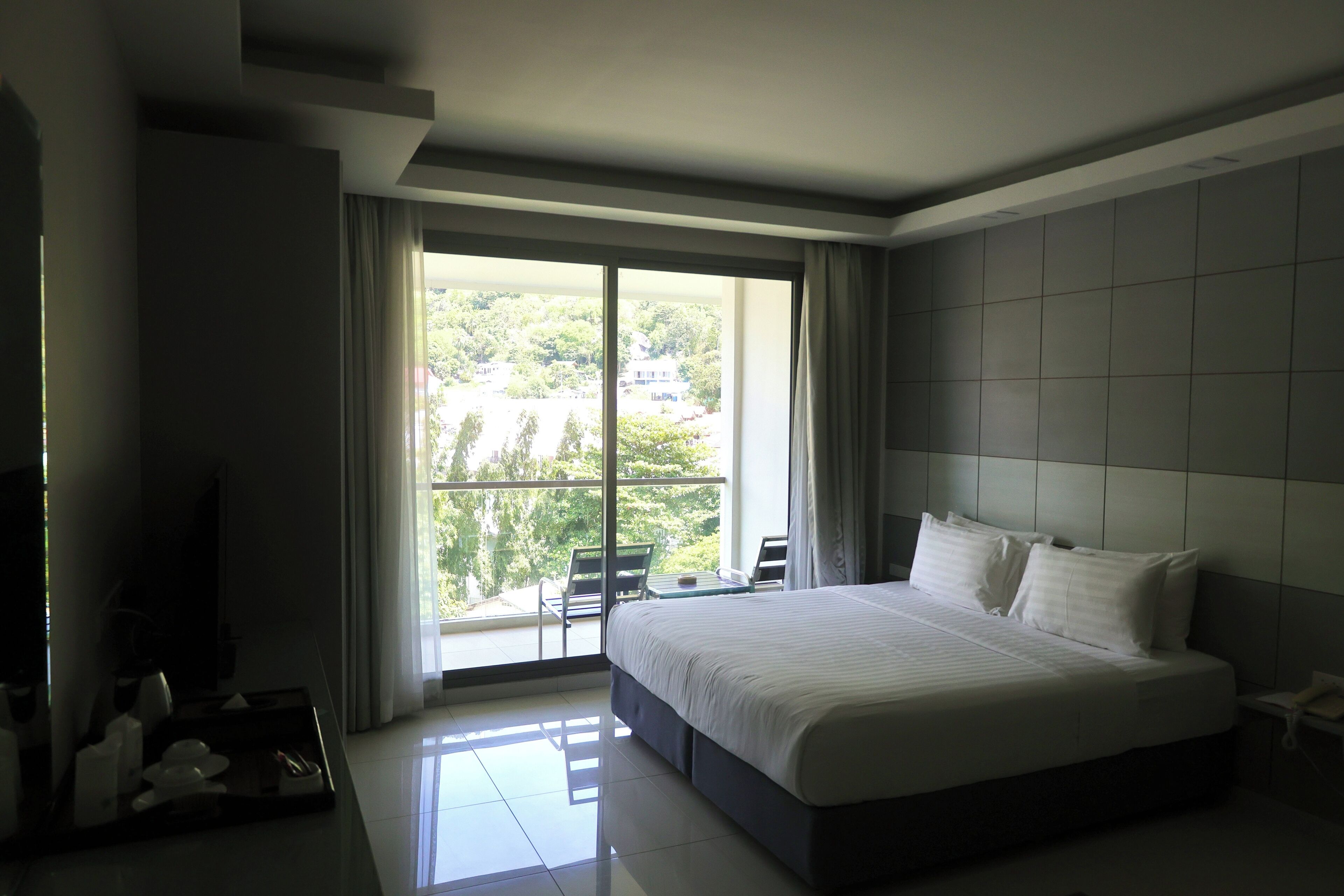 Una habitación de hotel moderna con una cama grande, un balcón con vistas a zonas verdes y un televisor de pantalla plana.