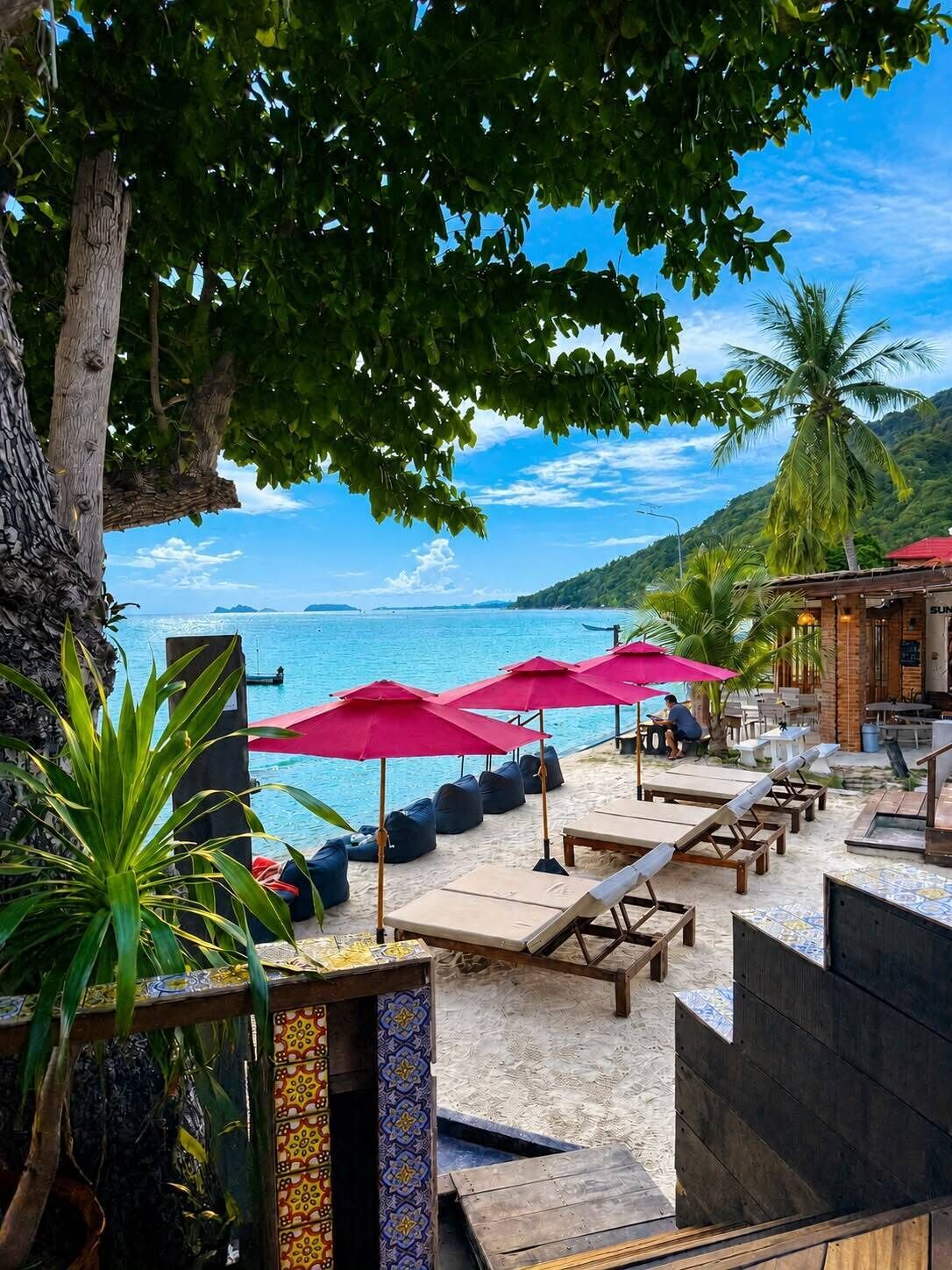 A beachside lounge area with sun loungers, umbrellas, and a pool.