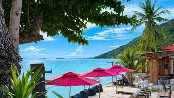 A beachside lounge area with sun loungers, umbrellas, and a pool.