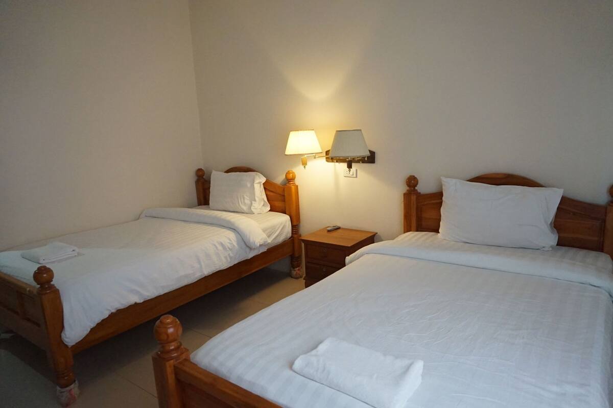 Two single beds with wooden headboards, a nightstand with a lamp, and a wall-mounted light fixture.