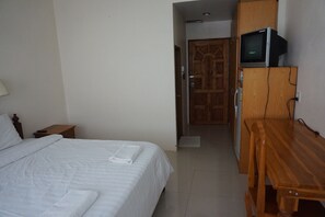 A hotel room with a bed, a wooden desk, a television on a cabinet, and a door leading to another room.