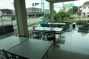 Uma área de estar interna com mesas e cadeiras, janelas amplas e vista para a rua.