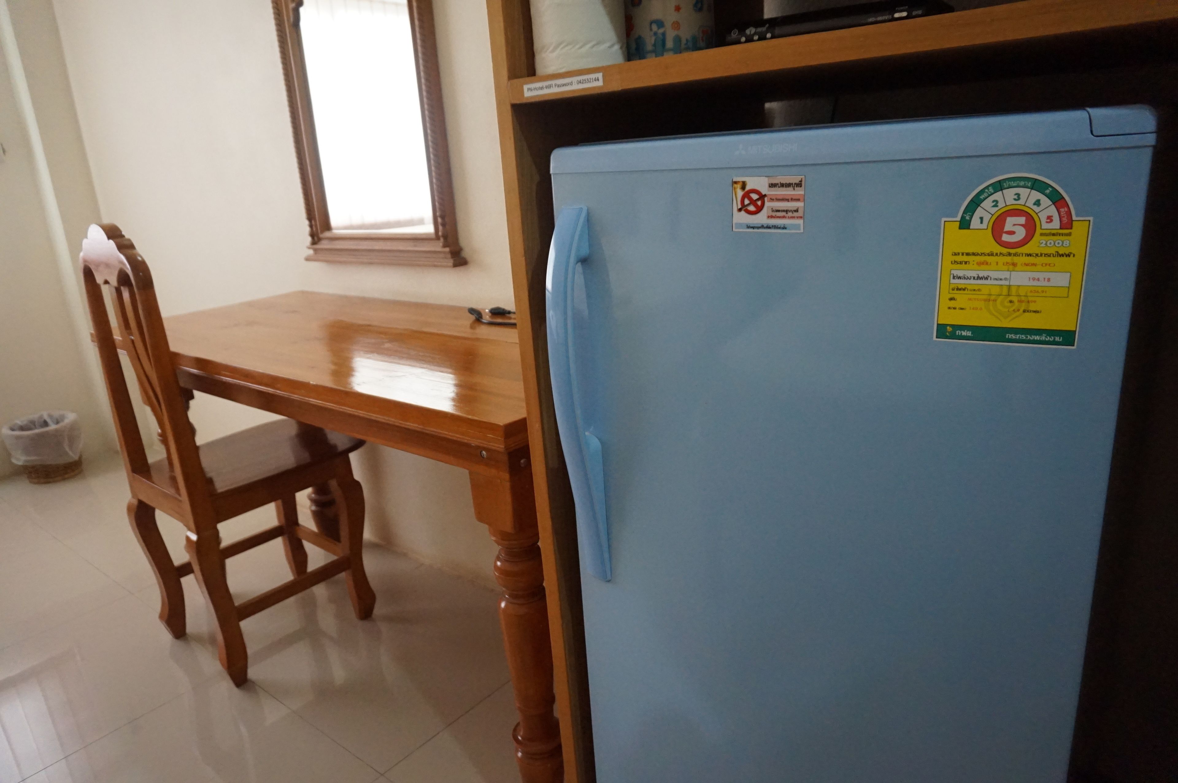 Una mesa de comedor de madera con una silla, un refrigerador azul con un adhesivo y una ventana con persianas.