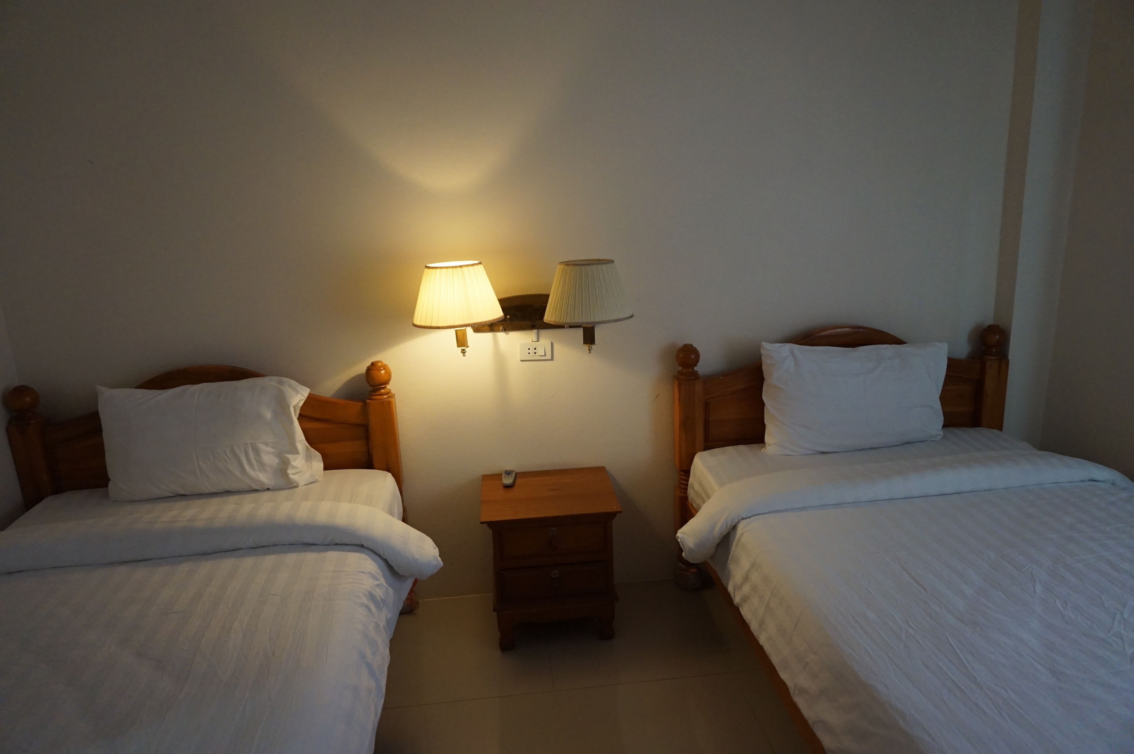Una habitación de hotel con dos camas individuales, una mesita de noche con lámpara y un pequeño aparador.