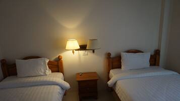 Una habitación de hotel con dos camas individuales, una mesita de noche con lámpara y un pequeño aparador.