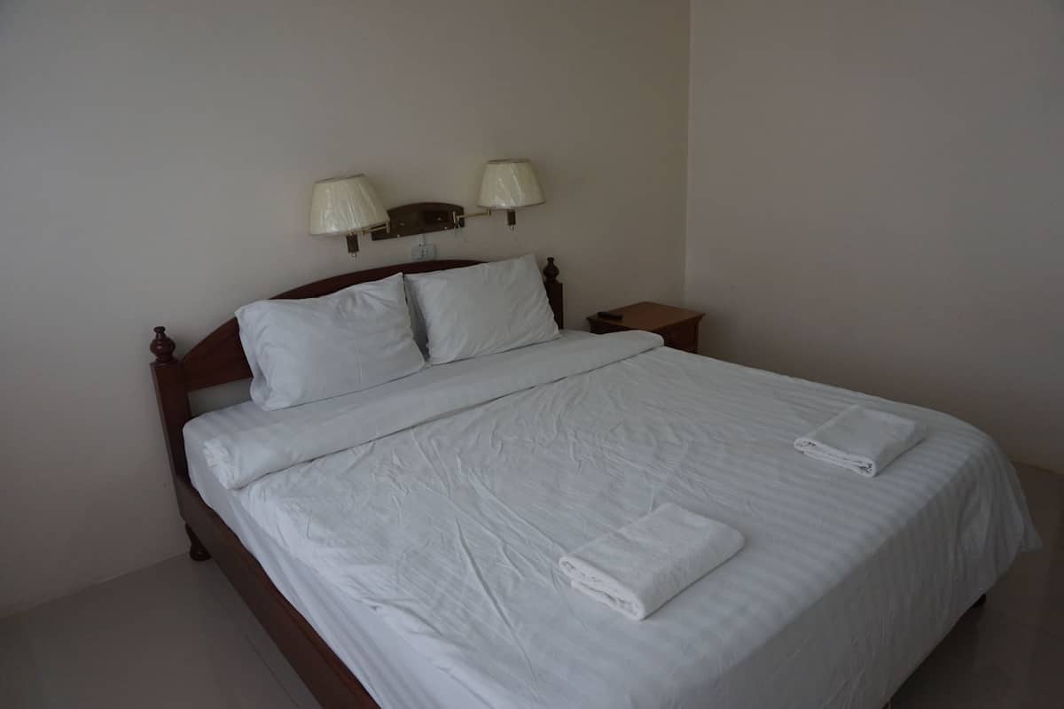 A neatly made bed with white linens and towels, a wooden headboard, two bedside lamps, and a small wooden nightstand.