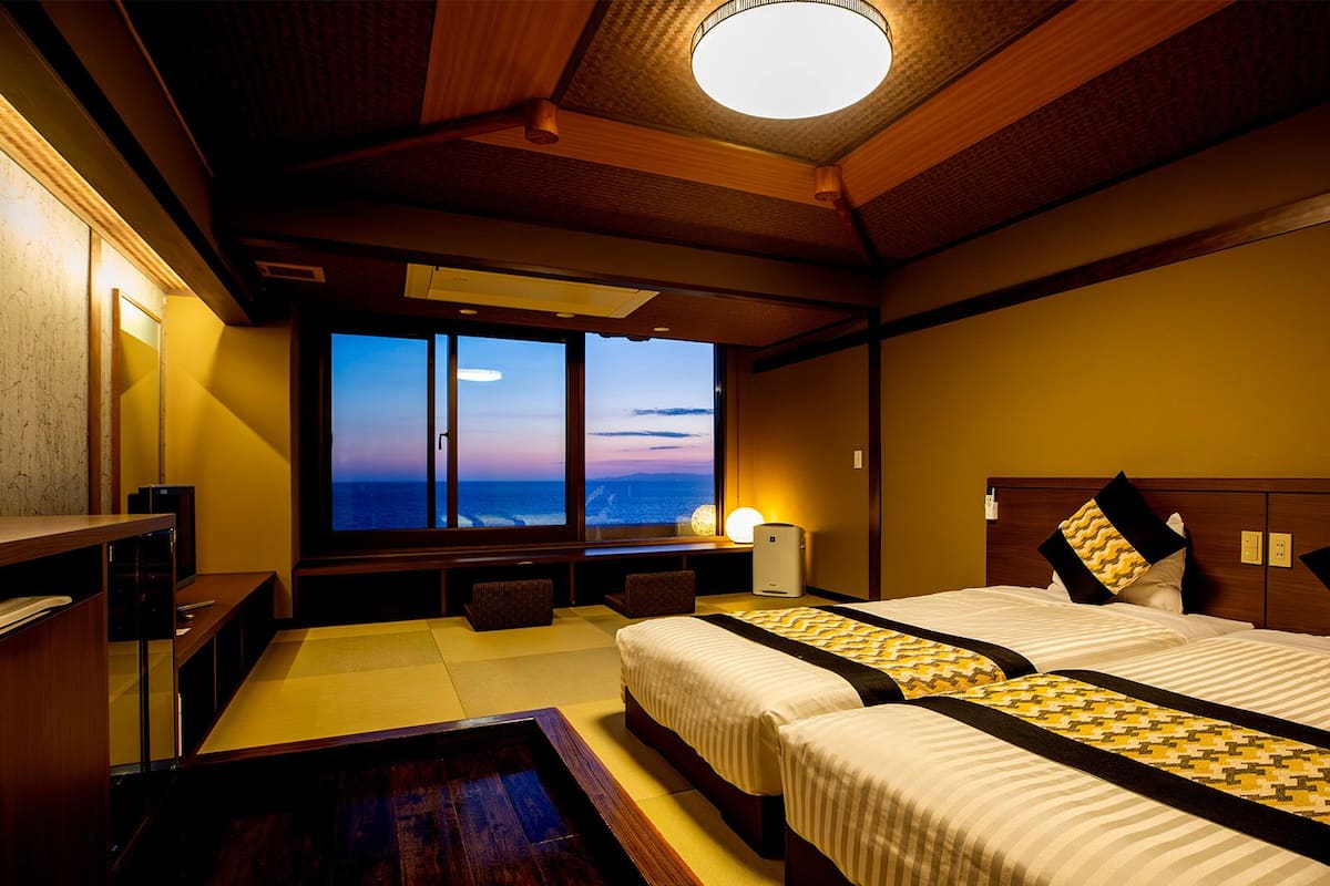 A hotel room with a large window, two beds, a desk, and a television.