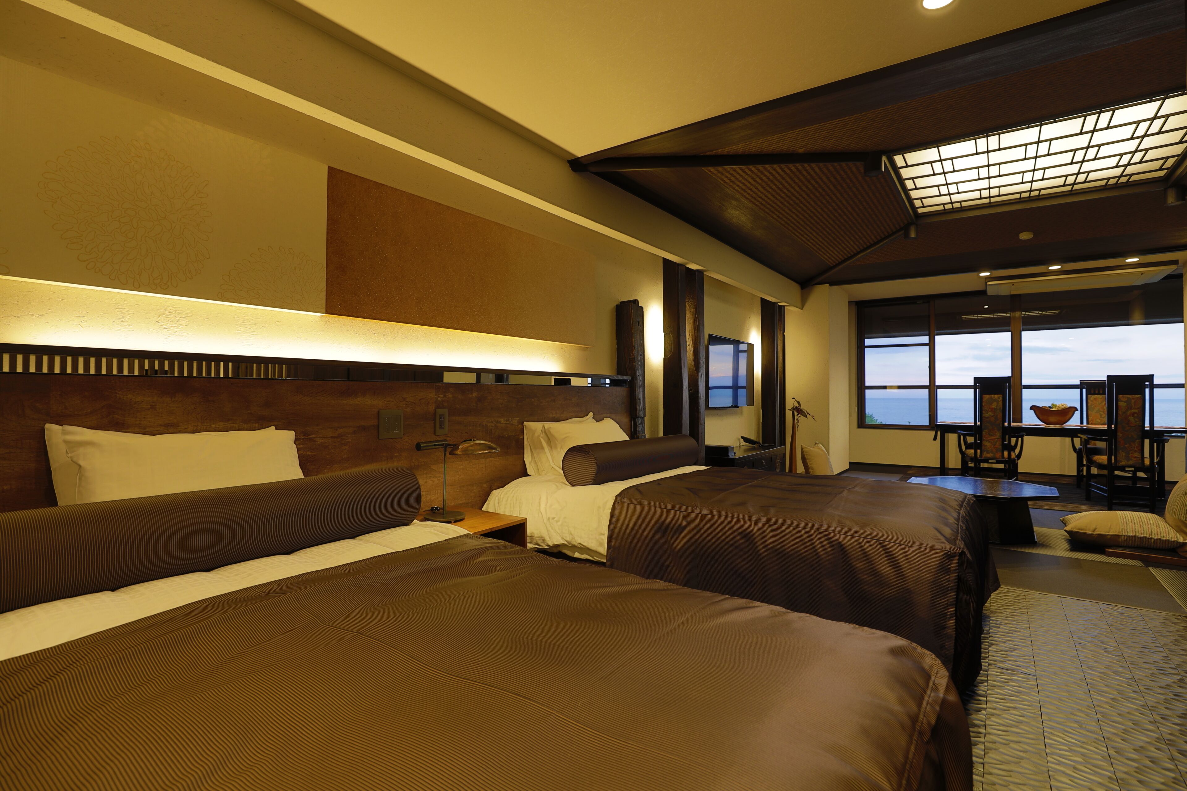 A hotel room with two beds, a dining area with a view, and a large window.