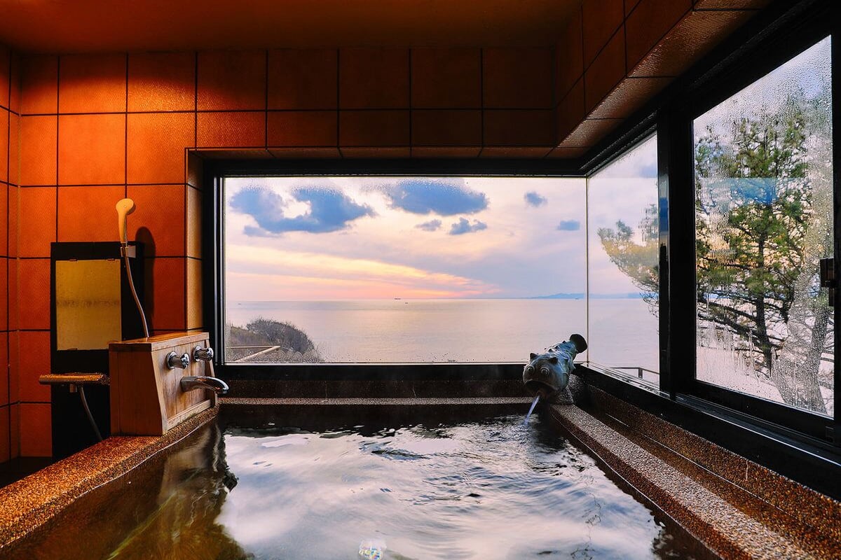 A hot tub with a view of the sea, a wooden cabinet, and a window.