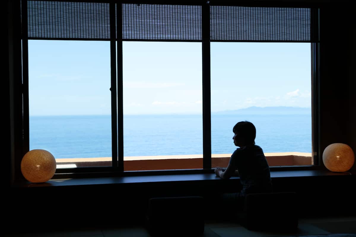 A room with a large window overlooking a beach and mountains.