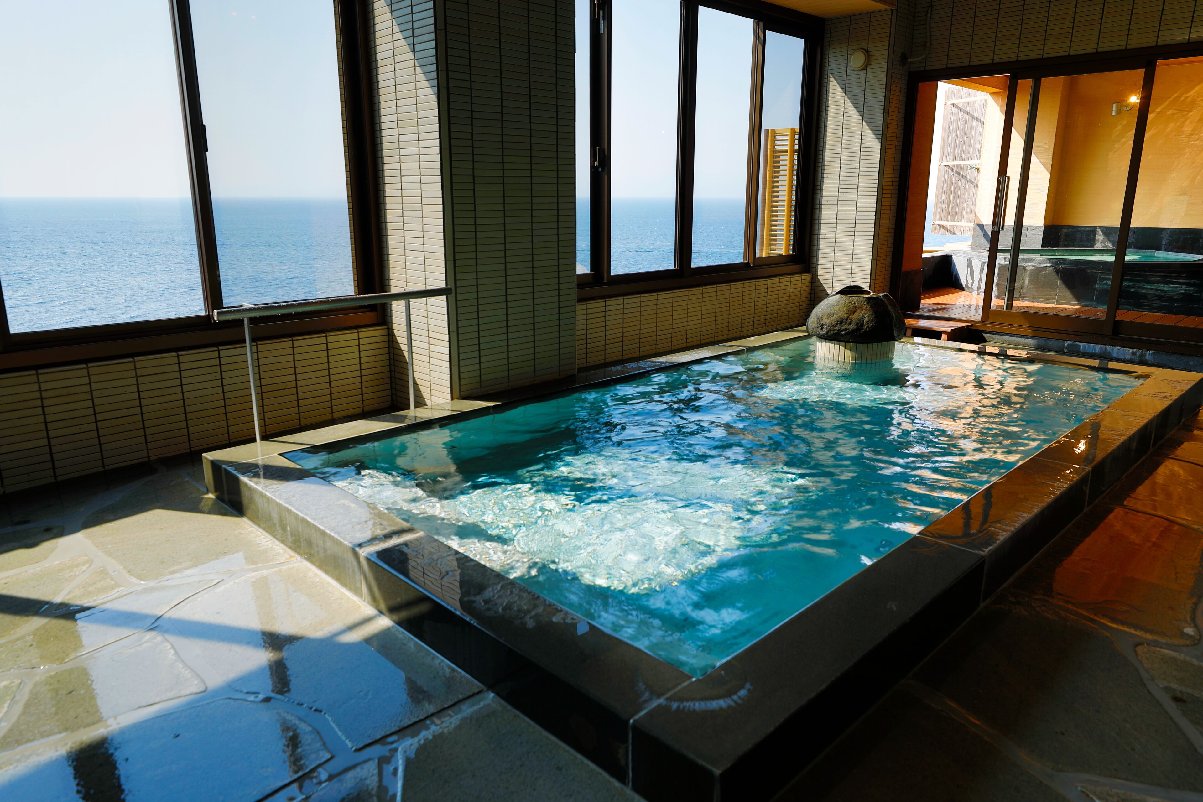 A hot tub with a view of the ocean through large windows.