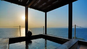 A glass-enclosed infinity pool with a view of the ocean and sunset. - Hotel Isaba (Numazu)