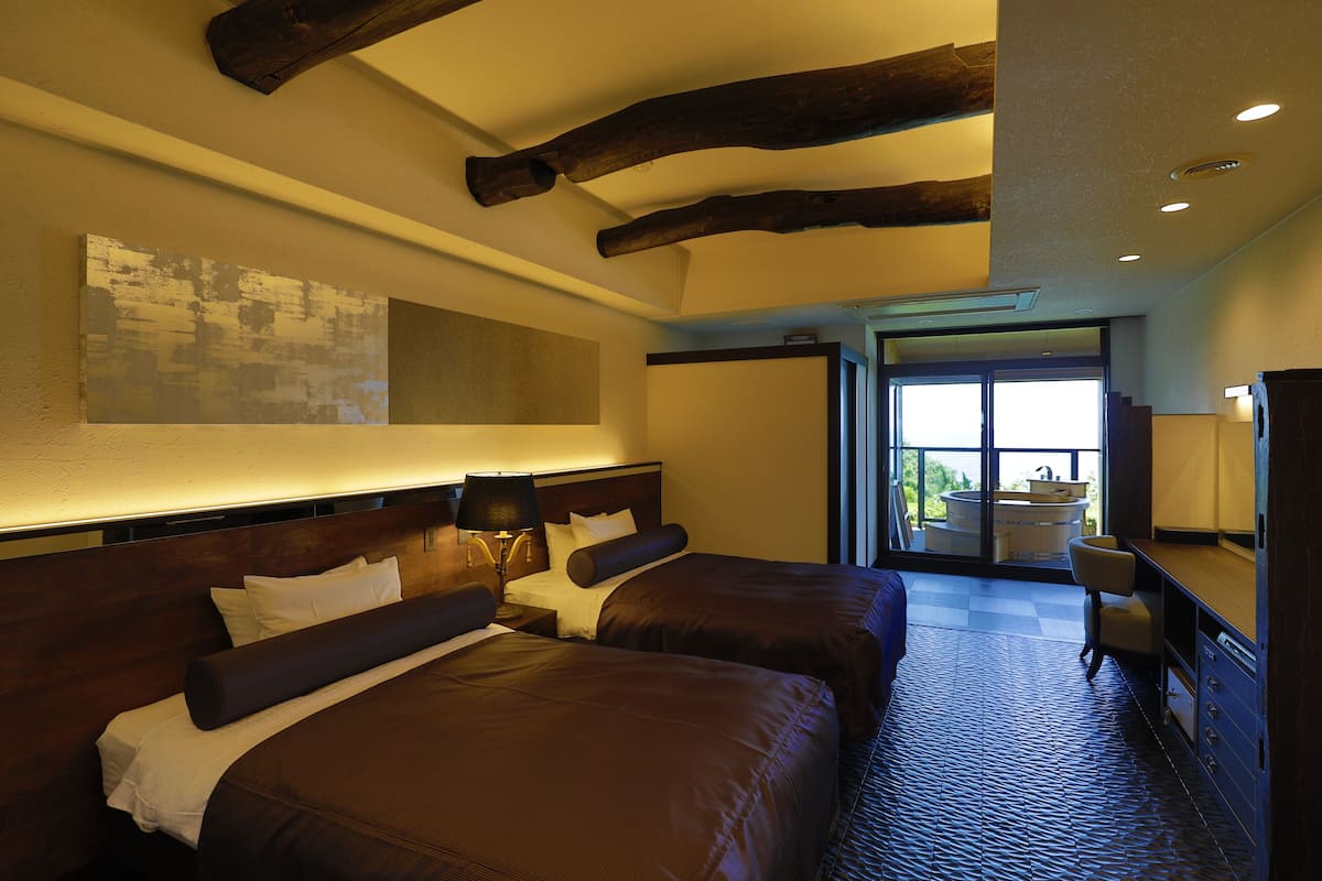A hotel room with two beds, a large mirror, a desk, and a bathroom visible through an open door.