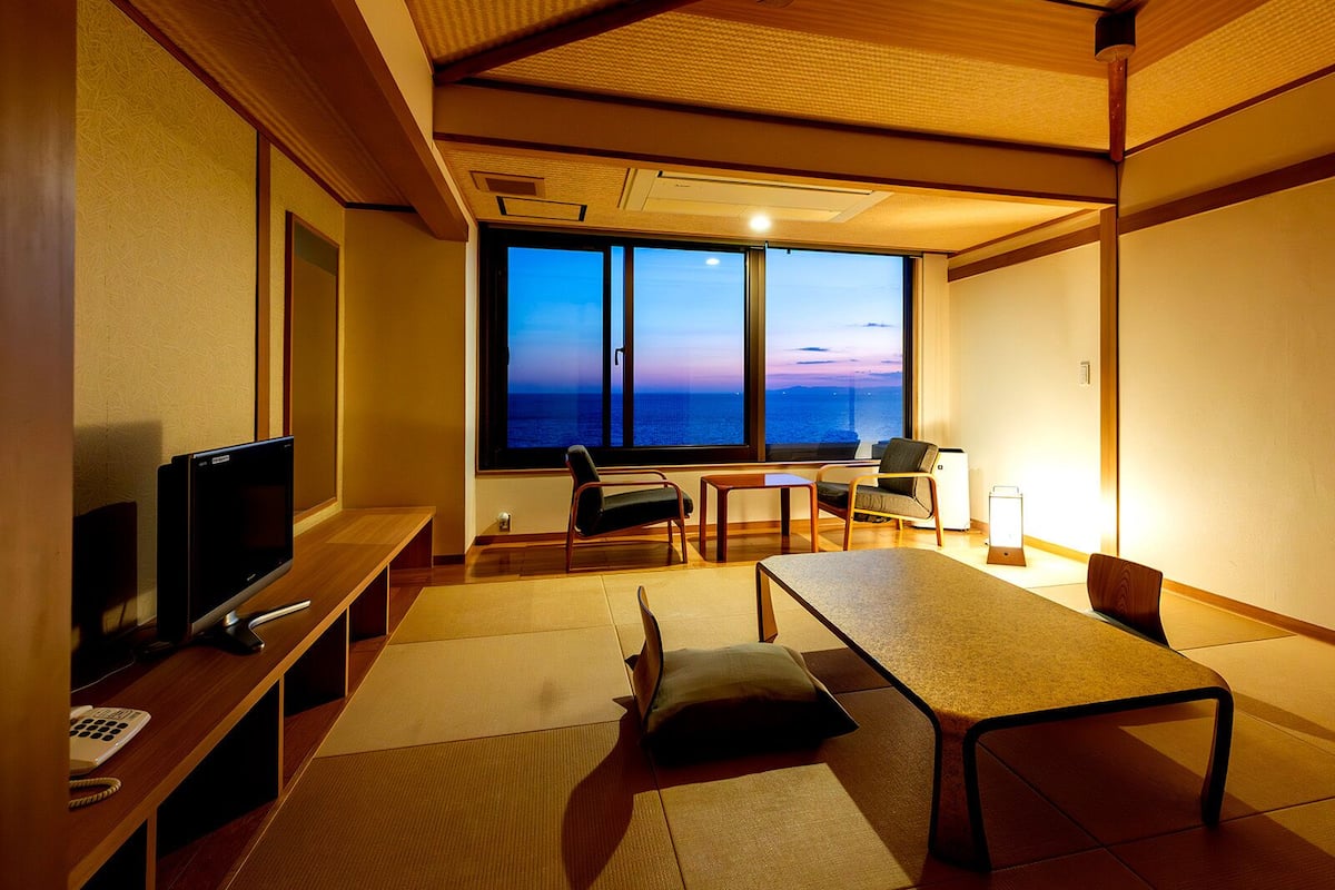 A room with a large window, a television, a table, and chairs.