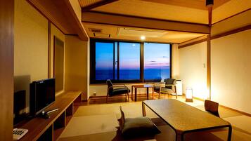 Una habitación con un ventanal grande, televisor, una mesa y sillas.