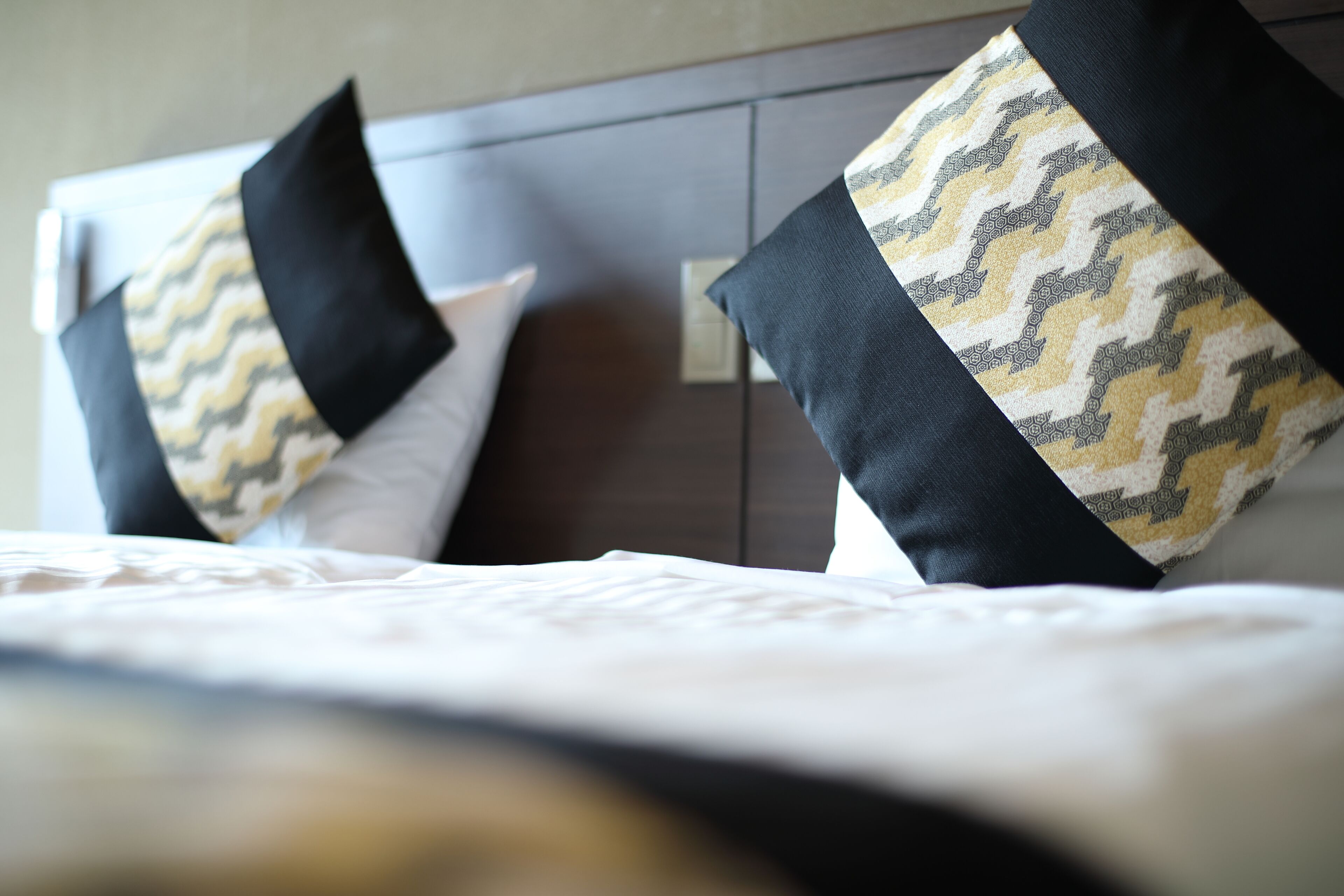 Ett hotellrum med en säng, två kuddar med ett sicksackmönster och en sänggavel i trä.