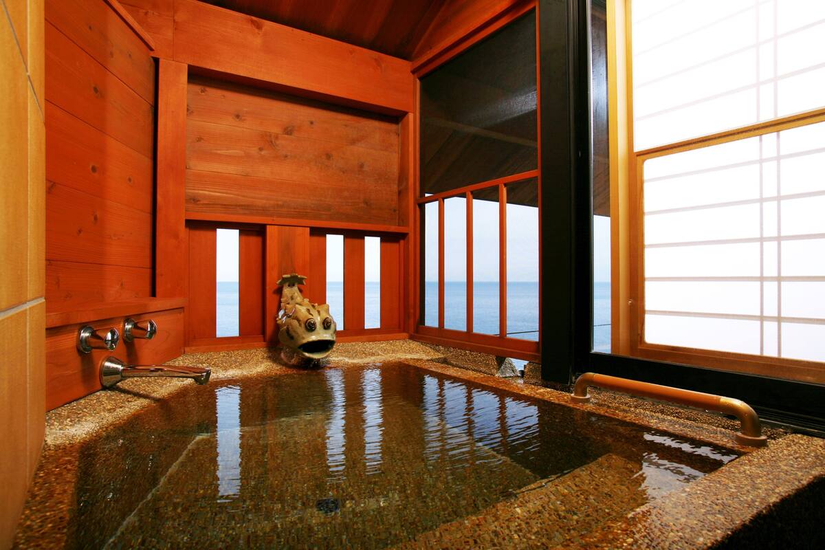 A wooden interior with a hot spring bath, wooden walls, and a large window with a view.