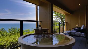 A hot tub with a view of the ocean, a table, and a sofa on a balcony.