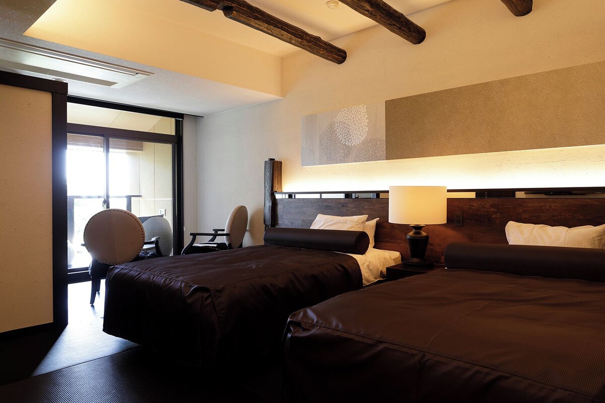 A hotel room with two beds, a desk, a chair, and a large window.