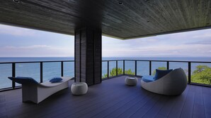 A modern outdoor seating area with a view of the sea, featuring a lounge chair and two round ottomans. - Hotel Isaba (Numazu)