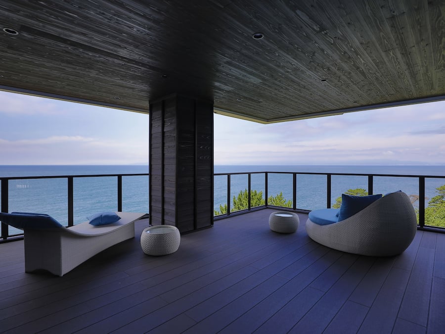 Ein moderner Außenbereich mit Meerblick, ausgestattet mit einer Liege und zwei runden Hocker.
