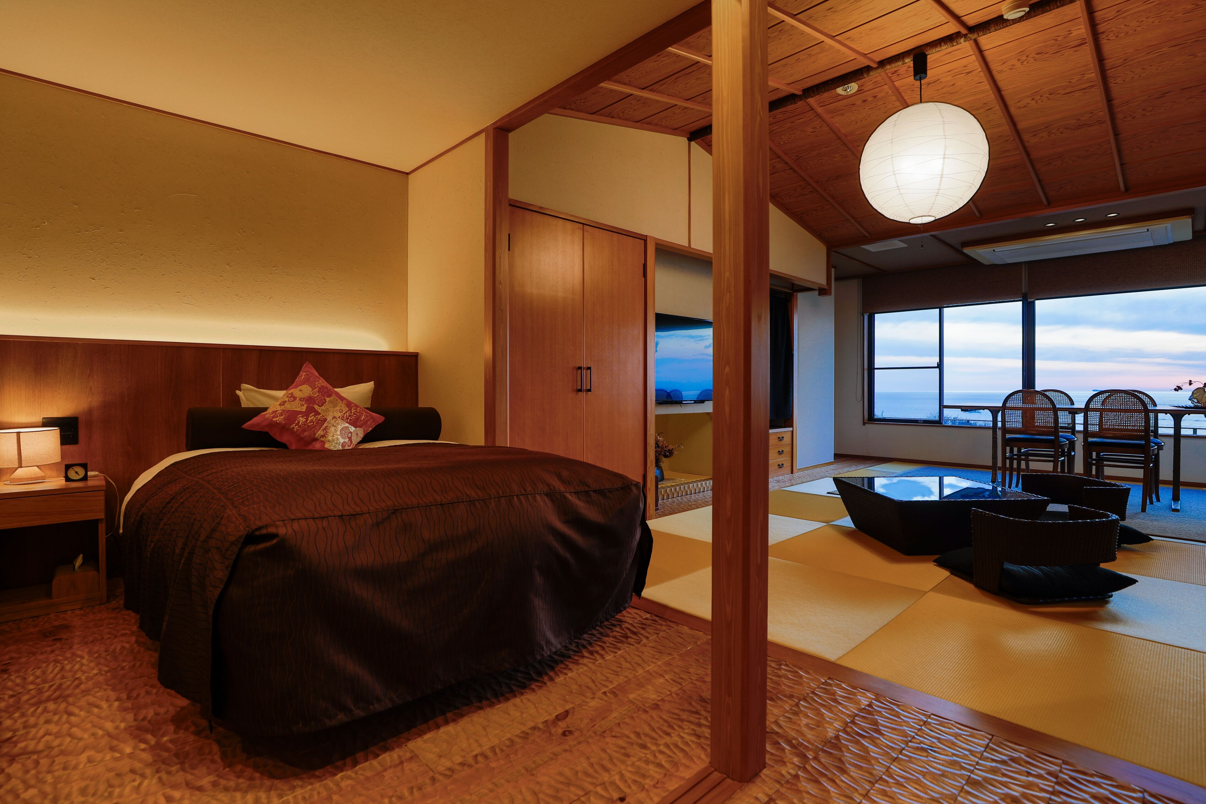 Een slaapkamer met een groot bed, houten plafond en uitzicht op zee door een groot raam.