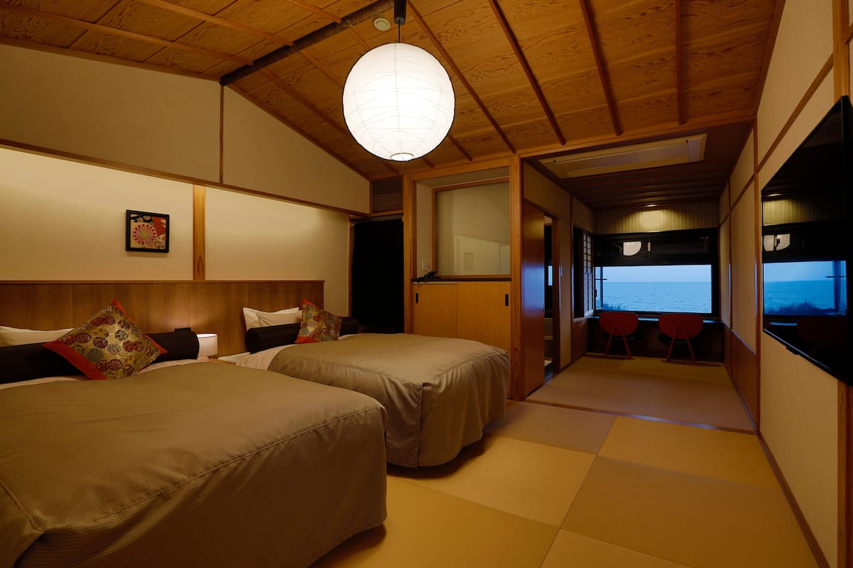 A room with two beds, a large window, and a view of the sea.