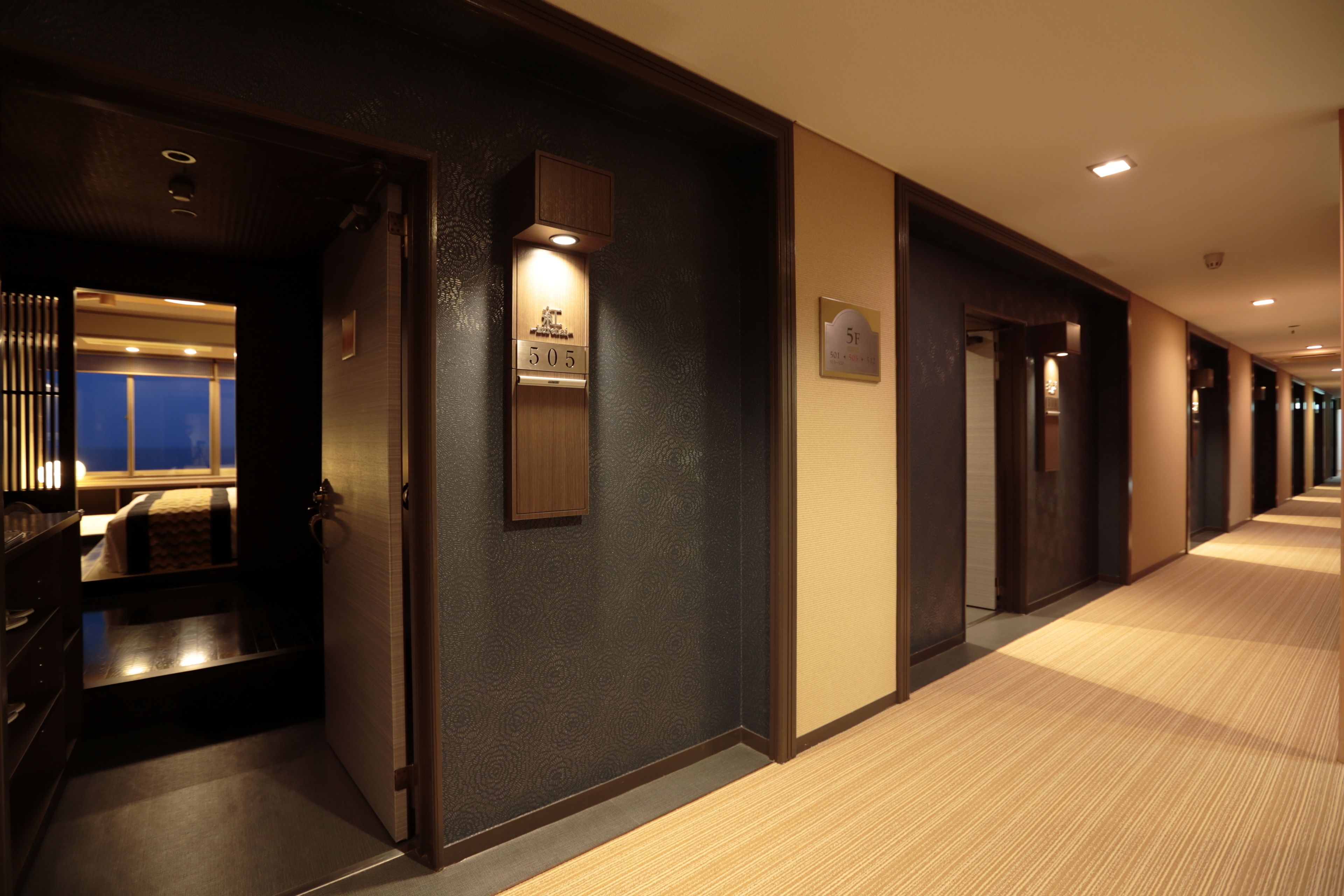 Un pasillo de hotel con una puerta de madera, un cartel con número y una lámpara.