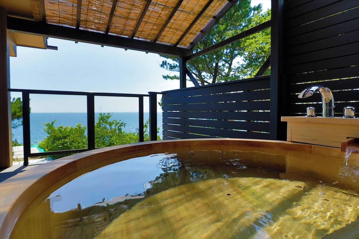 A hot tub with a view of the ocean, a wooden deck, and a metal railing.