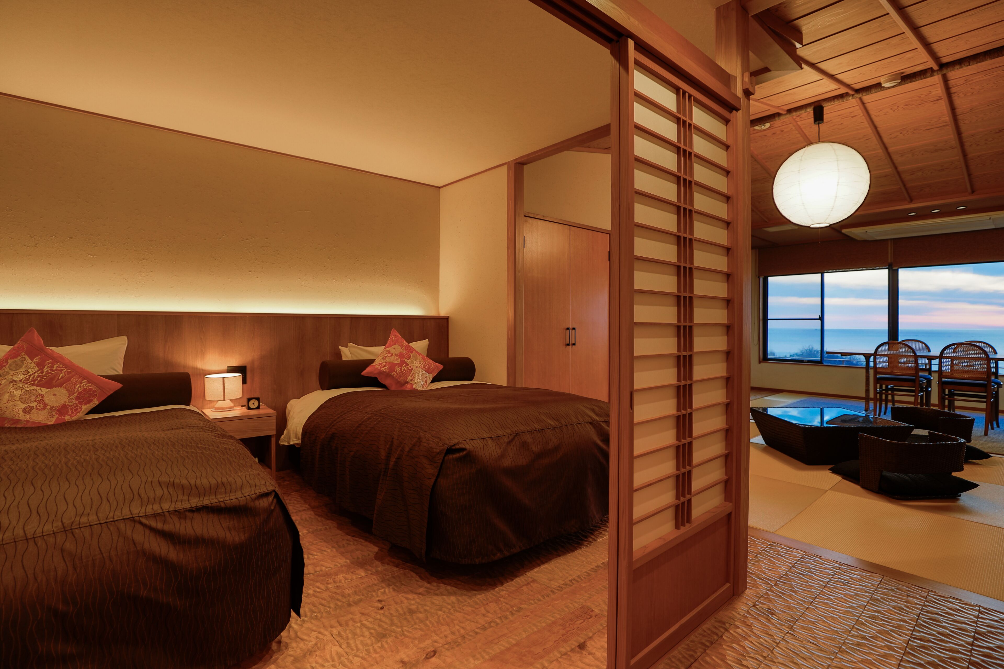 A hotel room with two beds, a view of the sea, and a traditional Japanese sliding door.